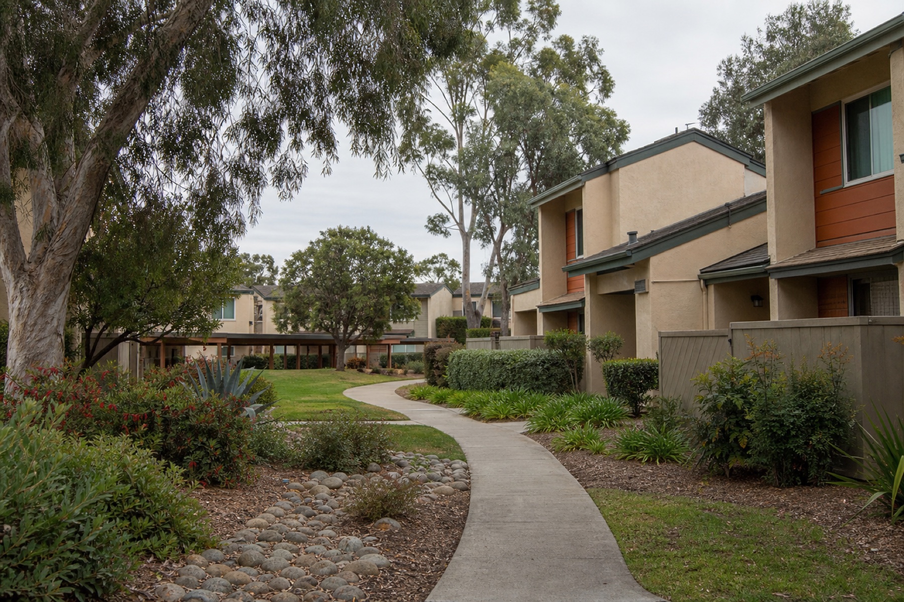 Shared walkway through an inland Carlsbad townhome and rental community beneath mature trees.