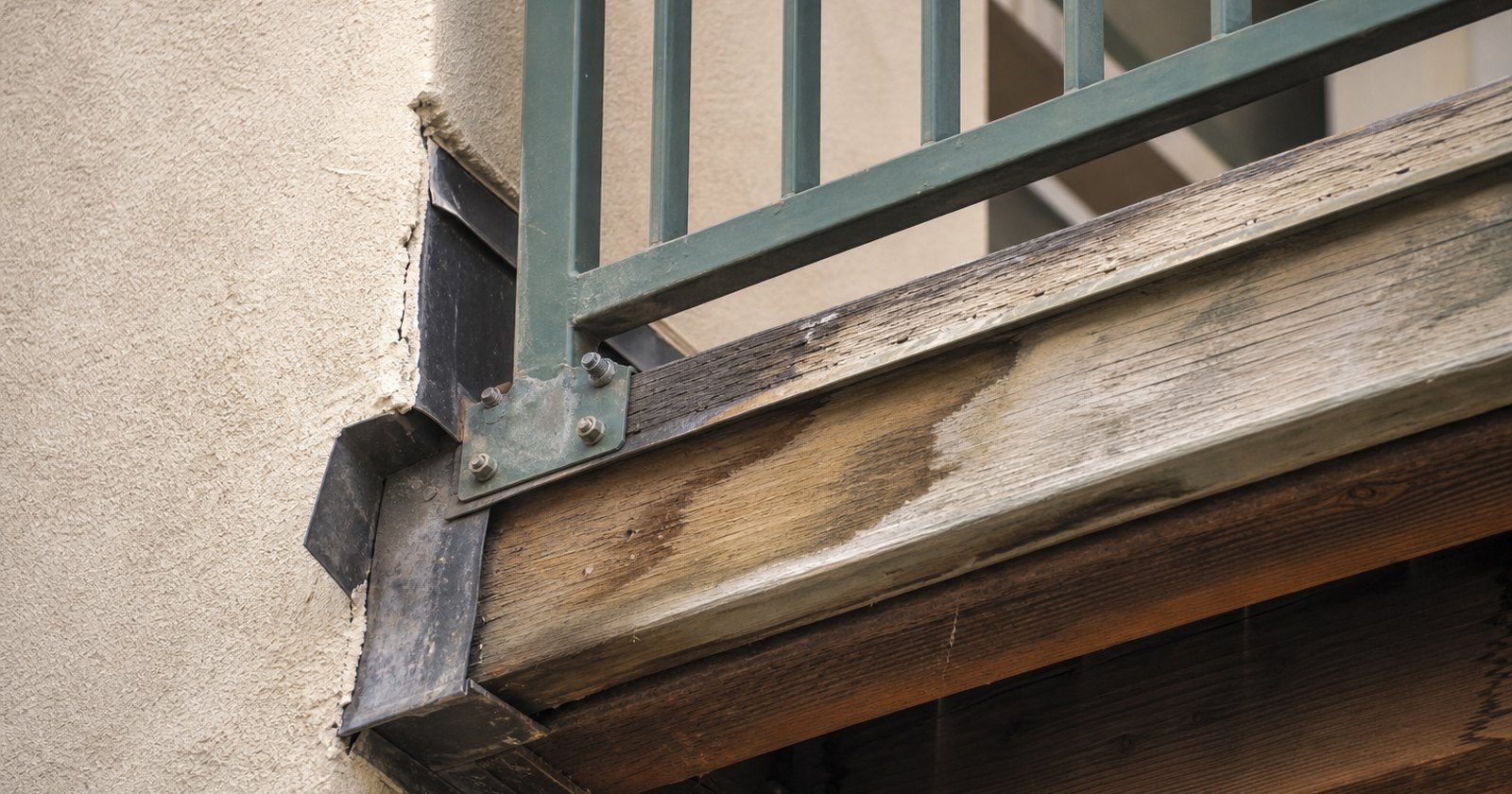 Close view beneath a balcony showing railing posts, ledger connection, and subtle moisture staining