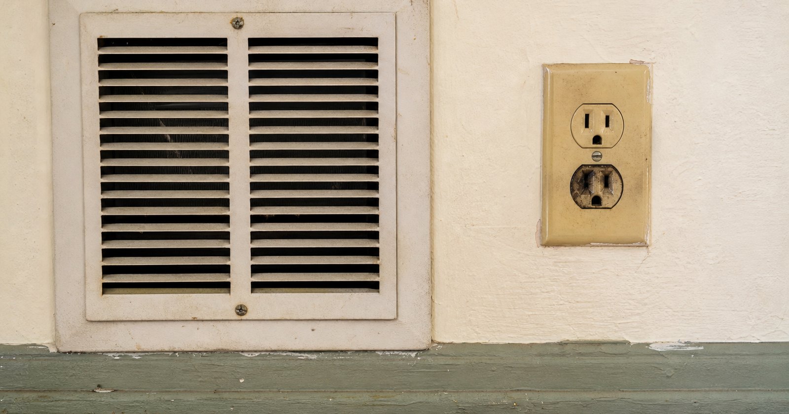 Old wall heater and scorched electrical outlet in a rental room awaiting professional repair